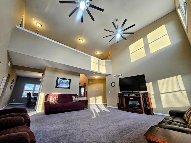 carpeted living area with a ceiling fan, baseboards, visible vents, and a high ceiling