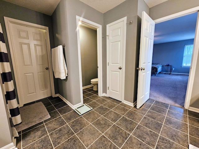 bathroom featuring toilet, tile patterned flooring, baseboards, and a textured ceiling