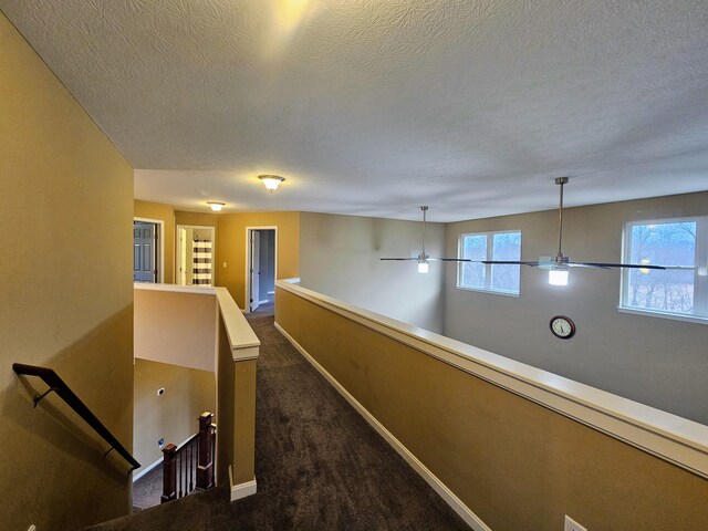 hallway featuring dark colored carpet, baseboards, a textured ceiling, and an upstairs landing