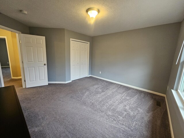 unfurnished bedroom with a textured ceiling, visible vents, baseboards, a closet, and dark colored carpet