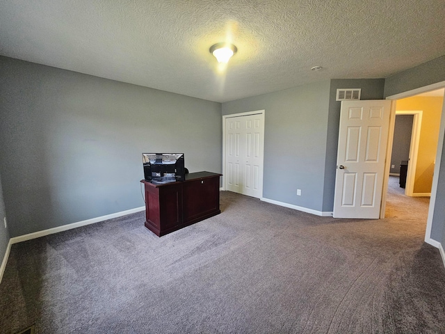 office area featuring a textured ceiling, dark carpet, visible vents, and baseboards