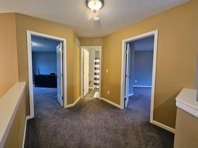 hallway with a textured ceiling, dark colored carpet, and baseboards