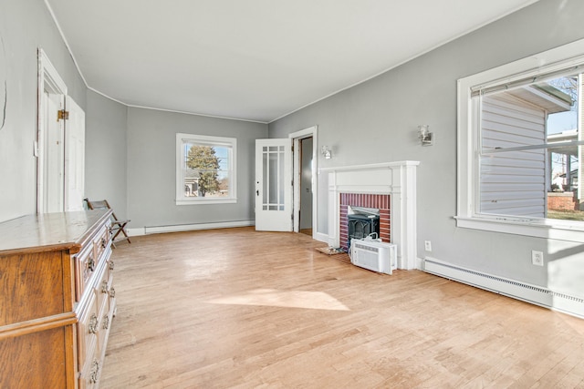 unfurnished living room with a healthy amount of sunlight, light wood-type flooring, and a baseboard heating unit