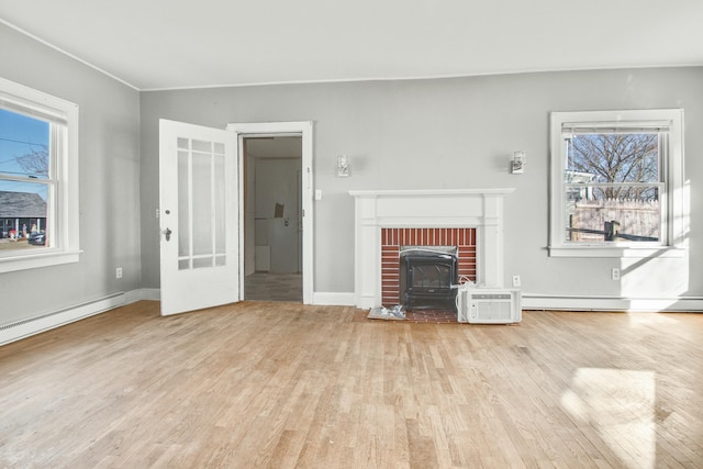 unfurnished living room featuring a wealth of natural light, a baseboard heating unit, and wood finished floors