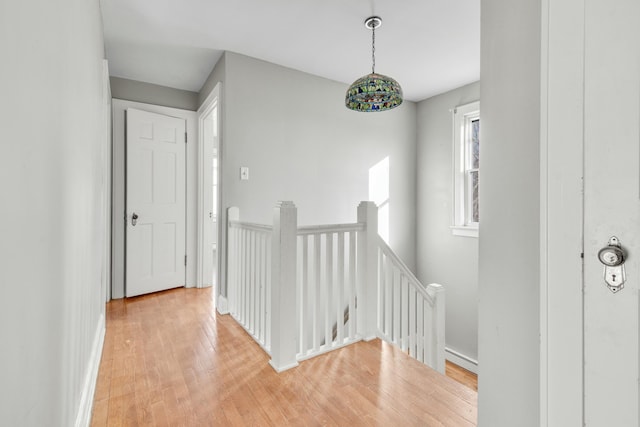 hall with light wood-type flooring, baseboards, and an upstairs landing