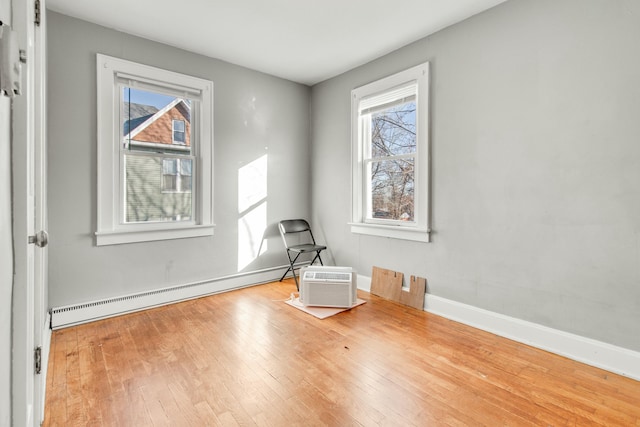 spare room featuring a wall unit AC, a baseboard radiator, wood-type flooring, and baseboards