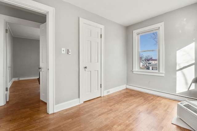 interior space with light wood-style floors, baseboards, baseboard heating, and a wall mounted air conditioner