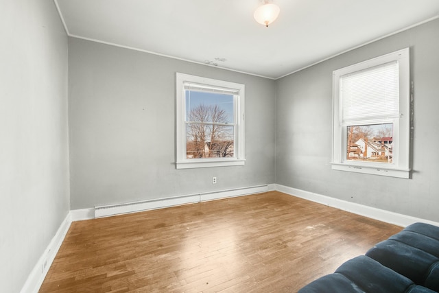 unfurnished room with a baseboard heating unit, crown molding, baseboards, and wood finished floors