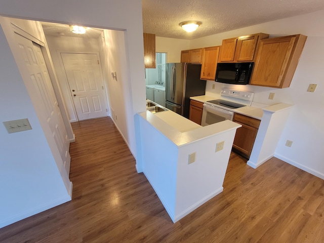 kitchen with white electric range, freestanding refrigerator, wood finished floors, washer and dryer, and black microwave