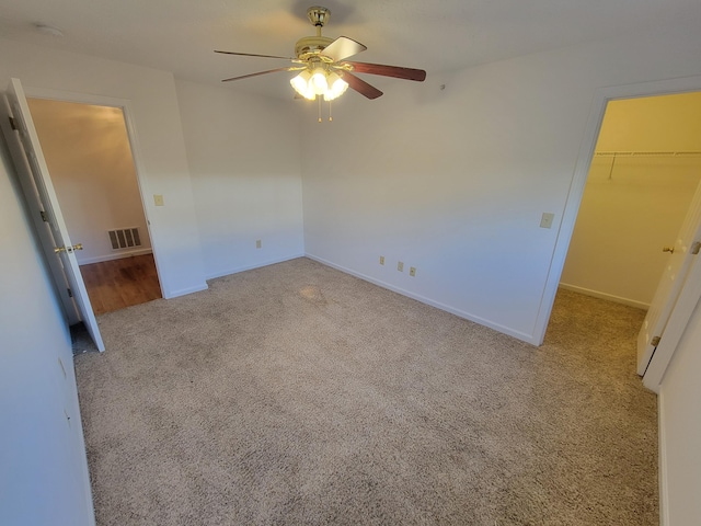 unfurnished bedroom with ceiling fan, carpet floors, visible vents, baseboards, and a walk in closet