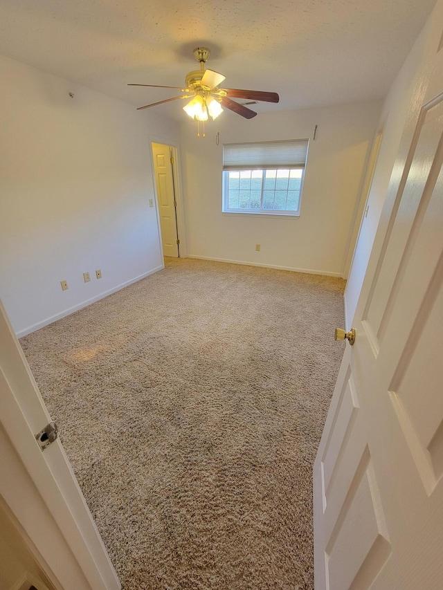 carpeted spare room with ceiling fan and baseboards