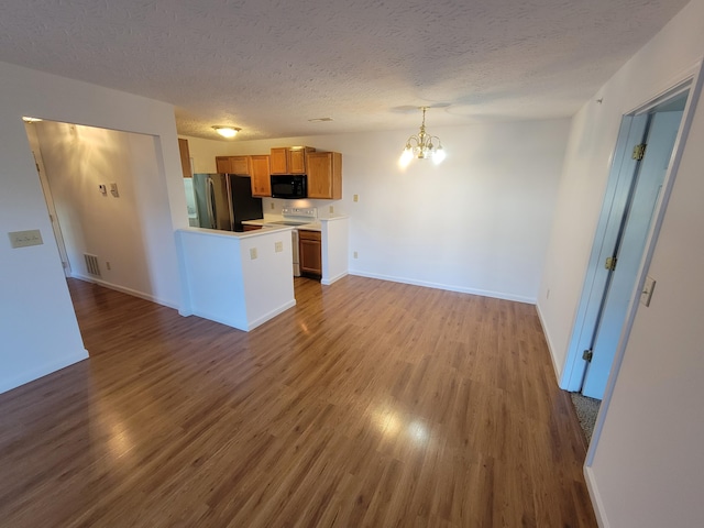 kitchen with brown cabinetry, electric range oven, wood finished floors, freestanding refrigerator, and black microwave