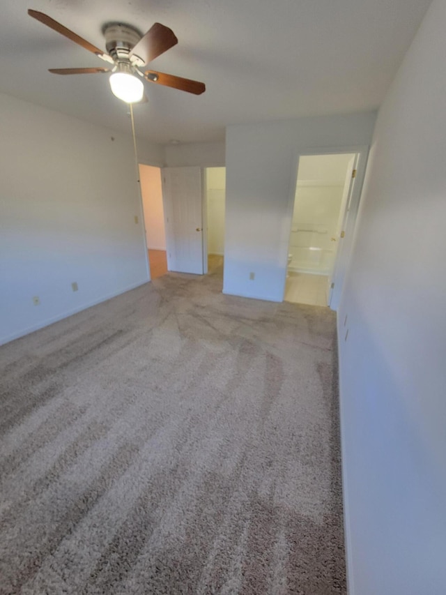 unfurnished bedroom featuring a ceiling fan, a walk in closet, light carpet, and connected bathroom