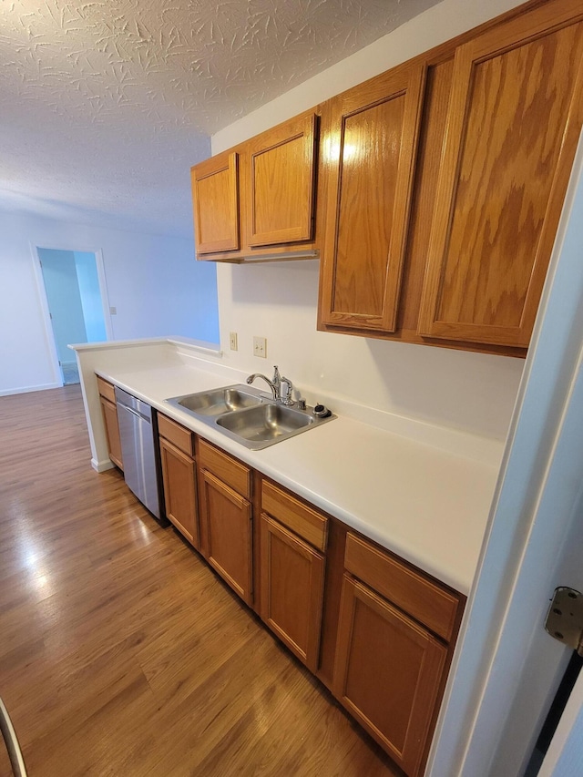 kitchen featuring brown cabinetry, light wood-style floors, a sink, and dishwasher