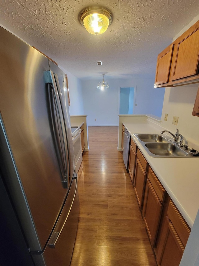 kitchen featuring a sink, light countertops, appliances with stainless steel finishes, light wood-type flooring, and brown cabinets