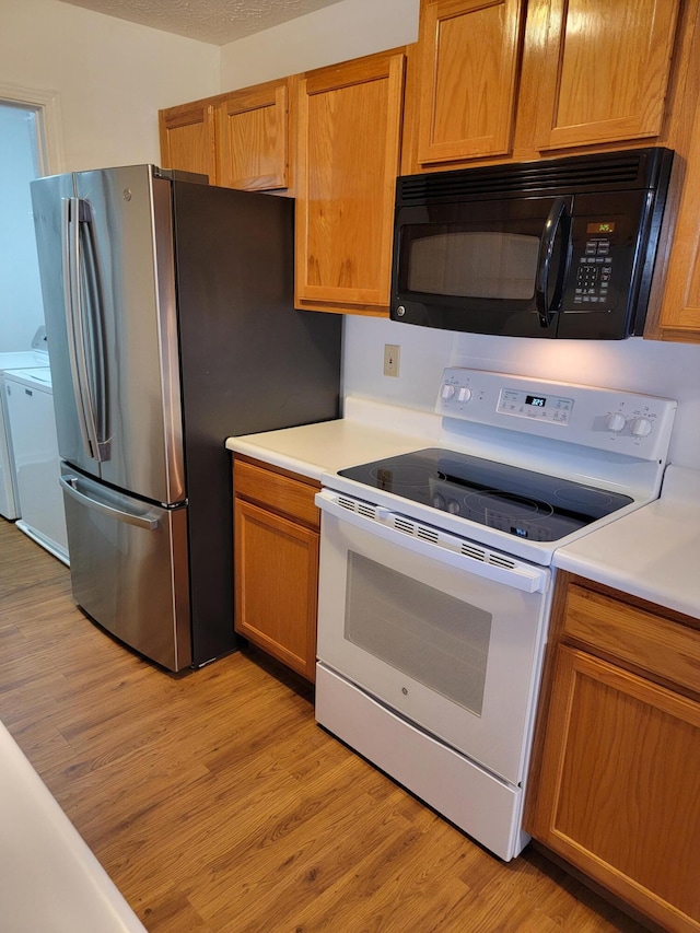 kitchen with white electric stove, black microwave, light wood-style floors, washer and dryer, and freestanding refrigerator