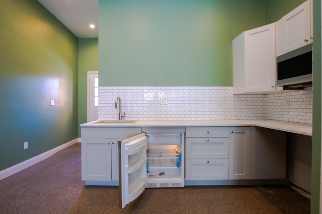 kitchen with white cabinets, stainless steel microwave, a sink, and backsplash