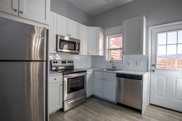kitchen featuring tasteful backsplash, light countertops, light wood-style flooring, appliances with stainless steel finishes, and a sink