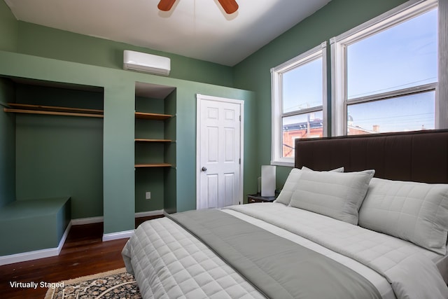 bedroom with wood finished floors, a ceiling fan, baseboards, a wall mounted air conditioner, and two closets