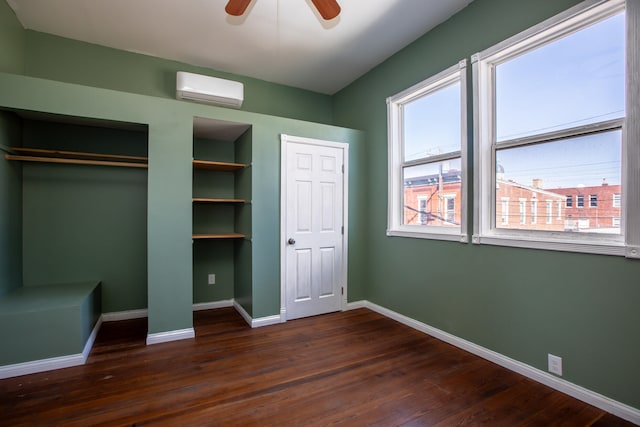 unfurnished bedroom featuring an AC wall unit, multiple windows, dark wood-style flooring, and two closets