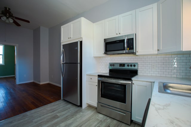 kitchen with light wood-style flooring, stainless steel appliances, a sink, white cabinets, and tasteful backsplash