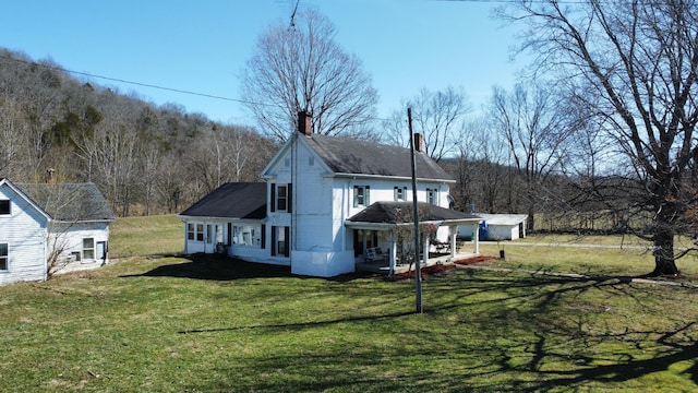 exterior space featuring driveway, a chimney, a front yard, and a wooded view