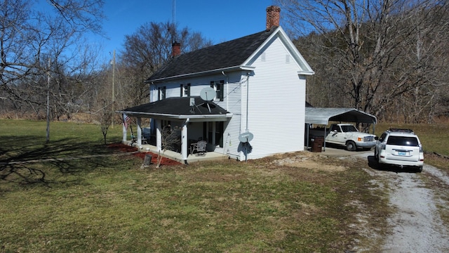 view of side of property with dirt driveway, a chimney, a lawn, and a detached carport