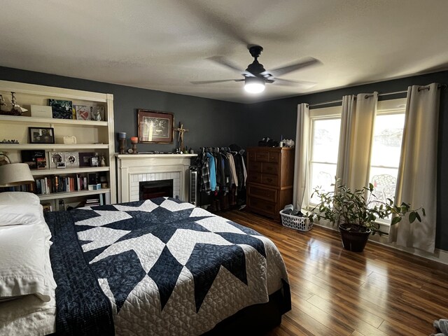 bedroom with a tile fireplace, wood finished floors, and a ceiling fan