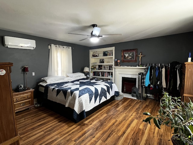 bedroom with ceiling fan, a wall mounted air conditioner, a fireplace, and wood finished floors