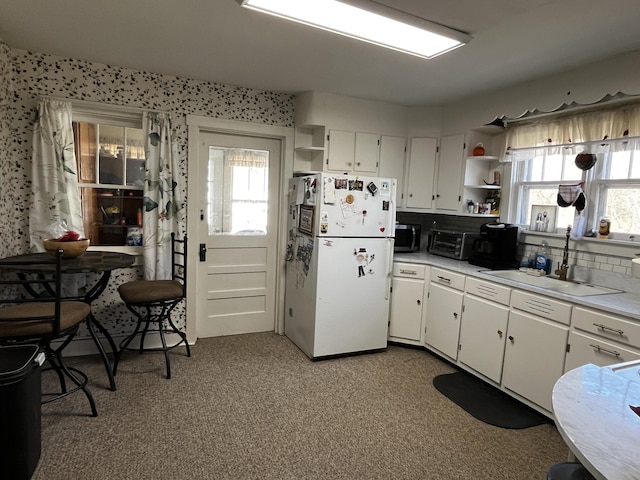 kitchen with open shelves, a wealth of natural light, stainless steel microwave, freestanding refrigerator, and a sink