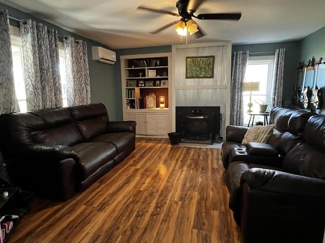 living area featuring built in features, ceiling fan, wood finished floors, a fireplace, and a wall mounted AC