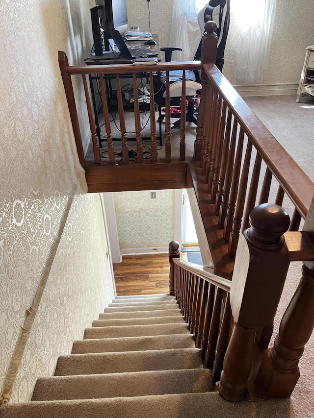 stairs featuring wood finished floors and wallpapered walls