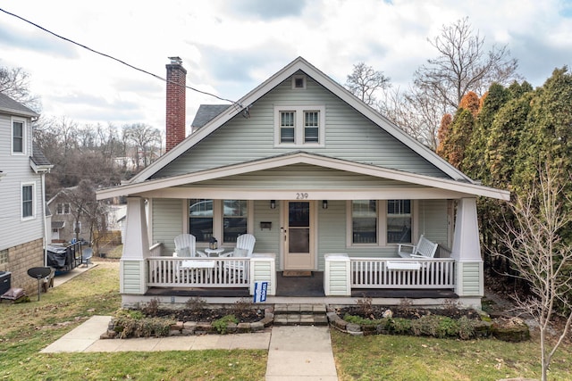 bungalow-style home with a porch, a chimney, and a front lawn