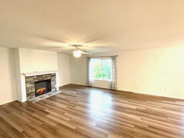 unfurnished living room featuring a ceiling fan, a fireplace, baseboards, and wood finished floors