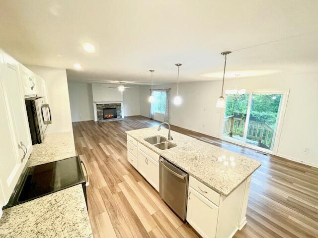 kitchen featuring range with electric cooktop, open floor plan, a sink, a stone fireplace, and stainless steel dishwasher