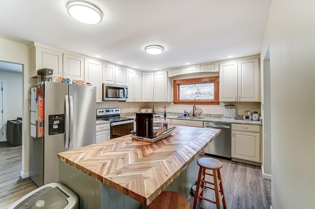 kitchen with stainless steel appliances, a sink, wood counters, white cabinetry, and a kitchen bar