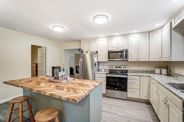 kitchen with a breakfast bar, stainless steel appliances, light wood-style flooring, white cabinetry, and a kitchen island