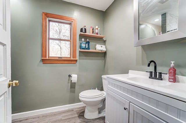 half bathroom with toilet, baseboards, wood finished floors, and vanity