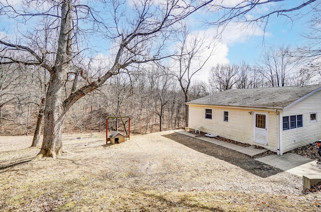 view of side of property with dirt driveway and roof with shingles