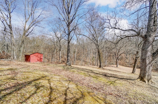 view of yard featuring a shed, a wooded view, and an outbuilding