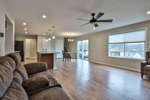 living room featuring baseboards, light wood finished floors, ceiling fan with notable chandelier, and recessed lighting