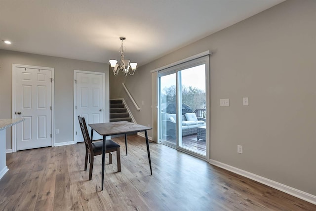 dining space featuring stairs, light wood-type flooring, an inviting chandelier, and baseboards