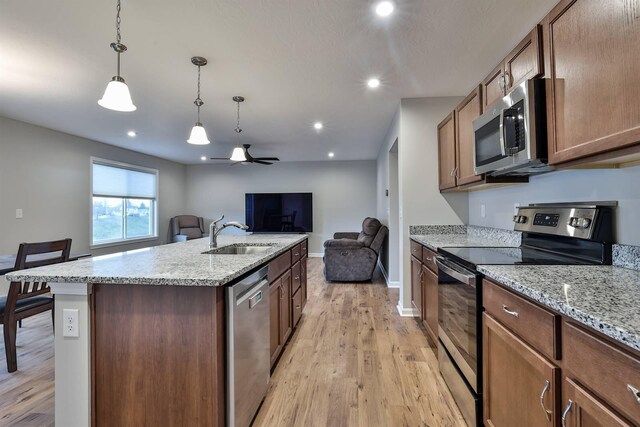 kitchen featuring light wood finished floors, stainless steel appliances, a ceiling fan, open floor plan, and a sink