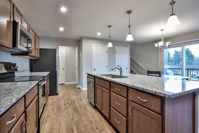 kitchen featuring pendant lighting, stainless steel appliances, light wood-style flooring, a sink, and baseboards