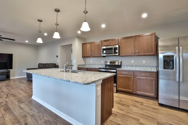 kitchen featuring stainless steel appliances, recessed lighting, a sink, light stone countertops, and light wood-type flooring