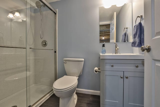 bathroom with toilet, wood finished floors, vanity, baseboards, and a shower stall