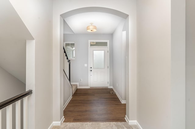 doorway with arched walkways, stairway, carpet flooring, and baseboards