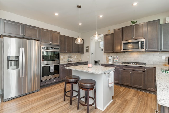 kitchen featuring a center island, light wood finished floors, appliances with stainless steel finishes, dark brown cabinets, and light stone countertops