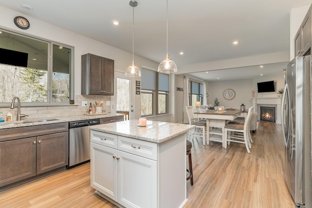 kitchen with light wood-style flooring, stainless steel appliances, a sink, open floor plan, and backsplash