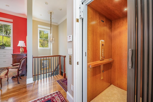 corridor with crown molding, an inviting chandelier, elevator, an upstairs landing, and wood finished floors